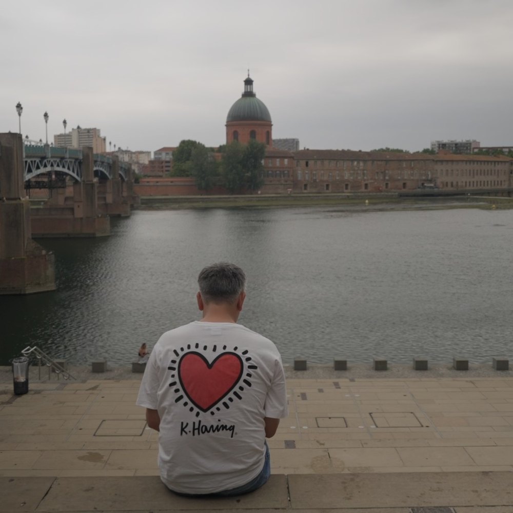 Melv assis sur les quais de la Garonne, de dos, face au dôme de la Grave